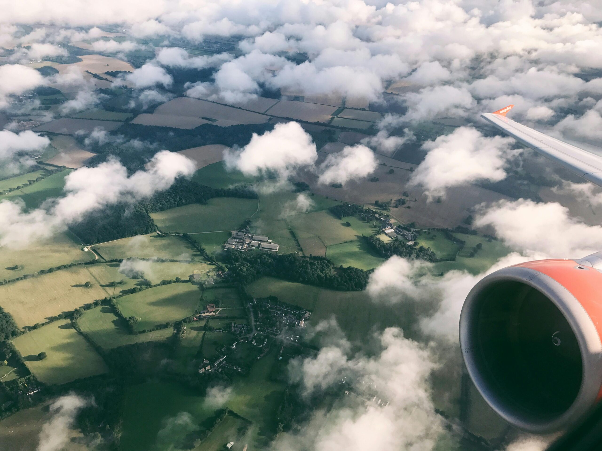 Scenic aerial view of the English countryside from an airplane window, showcasing landscapes and clouds.